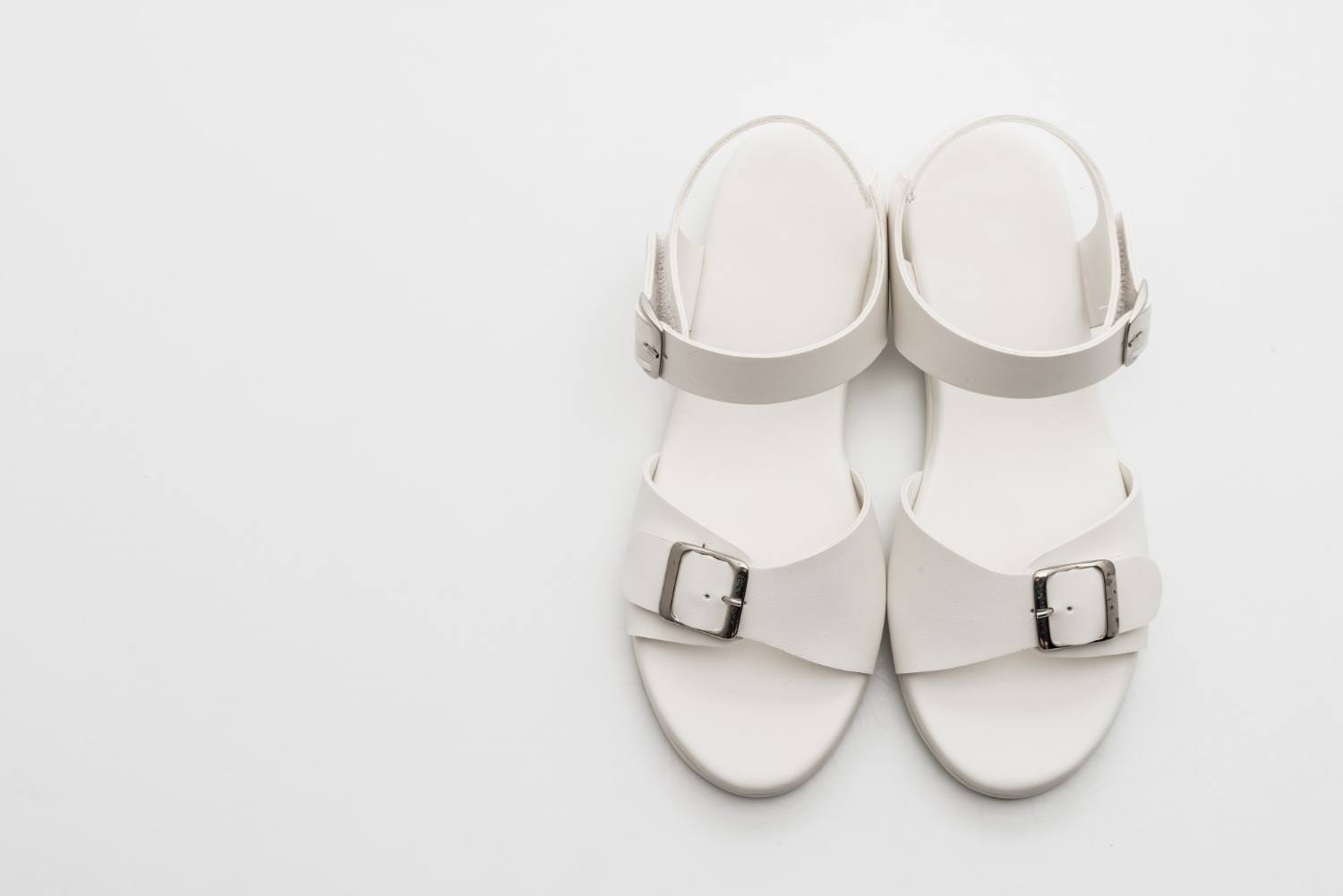 une paire de sandales blanches pour femme posées sur un fond bland